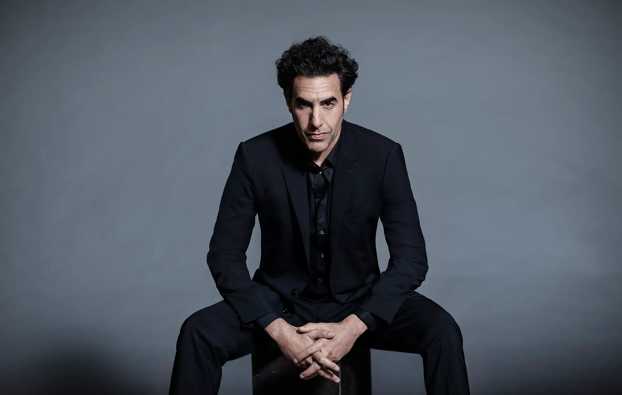 Sacha Baron Cohen, seated portrait in a dark suit, LA Times shoot, November 2020.