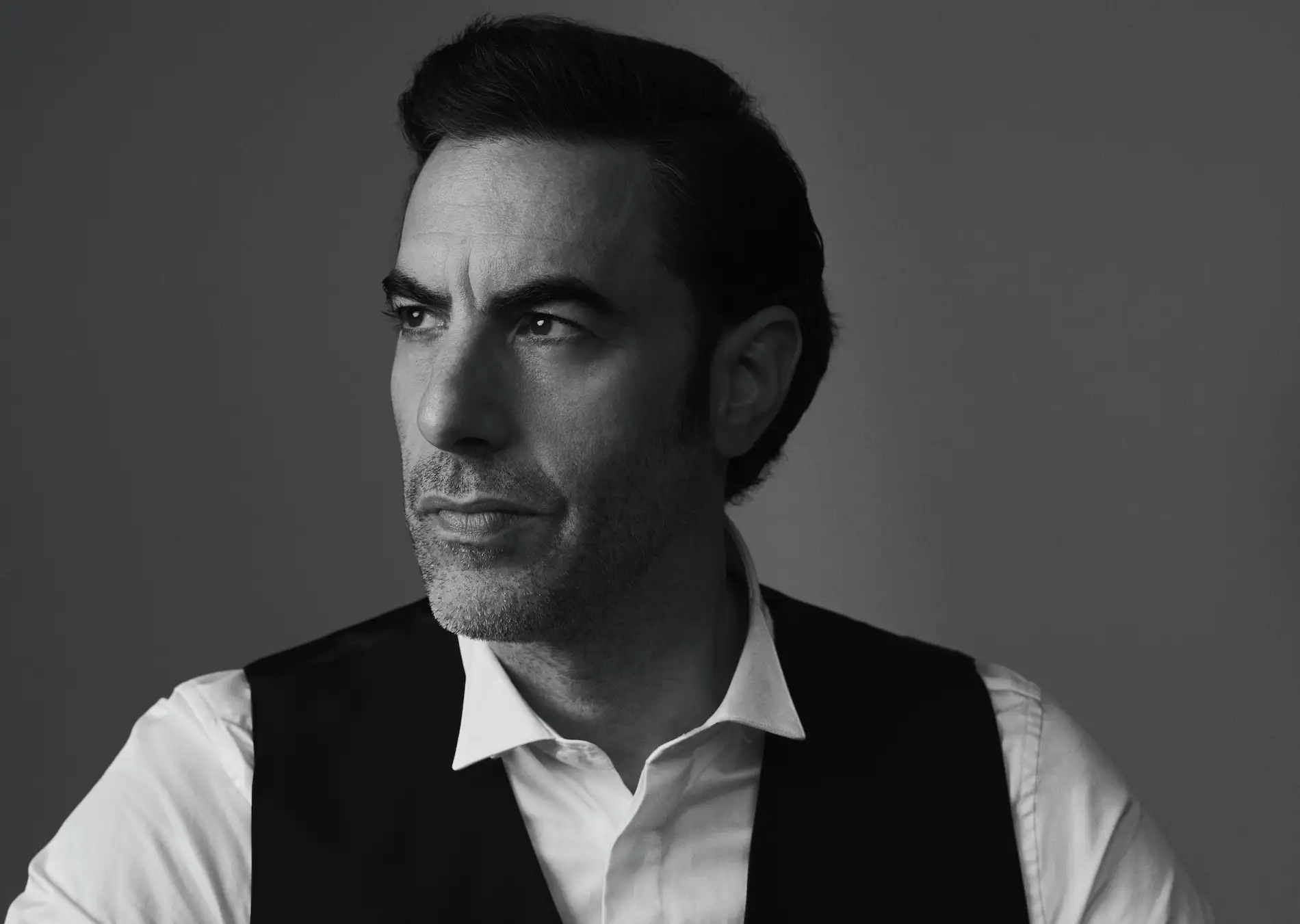 Sacha Baron Cohen, black-and-white studio portrait in a waistcoat, Backstage, October 2020.