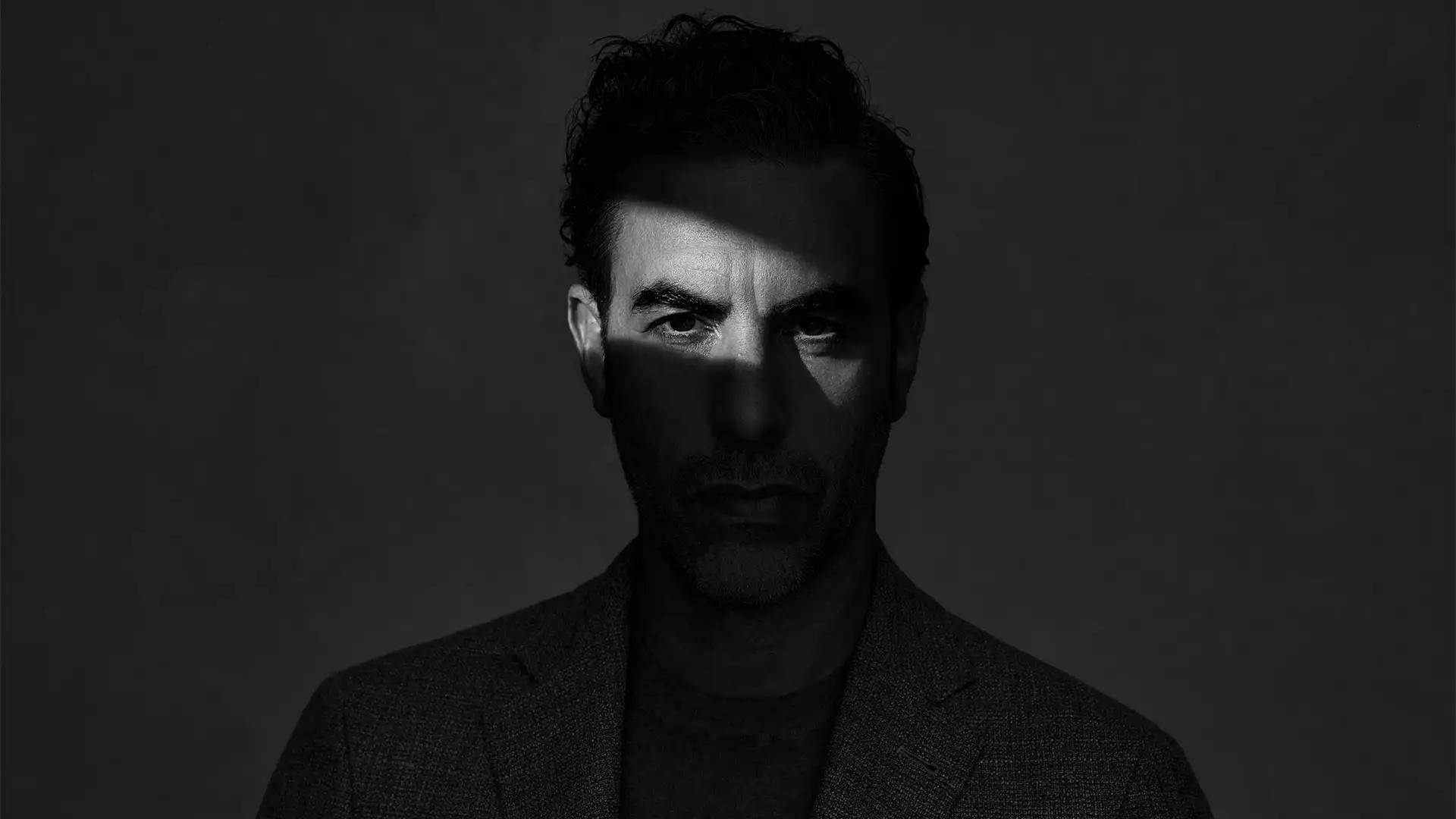 Sacha Baron Cohen, black-and-white portrait with a band of light across the eyes, Variety, December 2020.